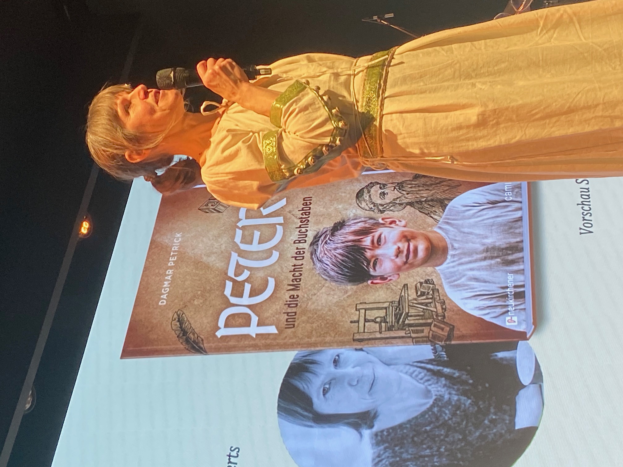 ©Jürgen Bublitz Die Autorin im mittelalterlichen Gewand vor dem Cover von Peter und die Macht der Buchstaben